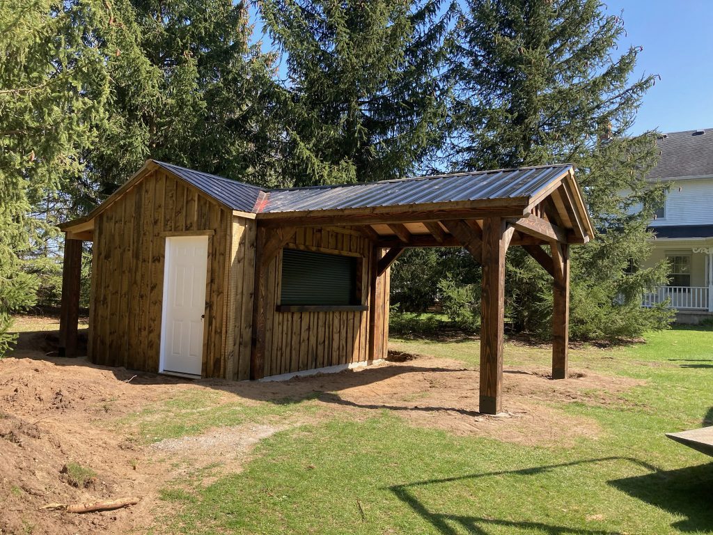 Backyard shed with role up window and third gable covered porch